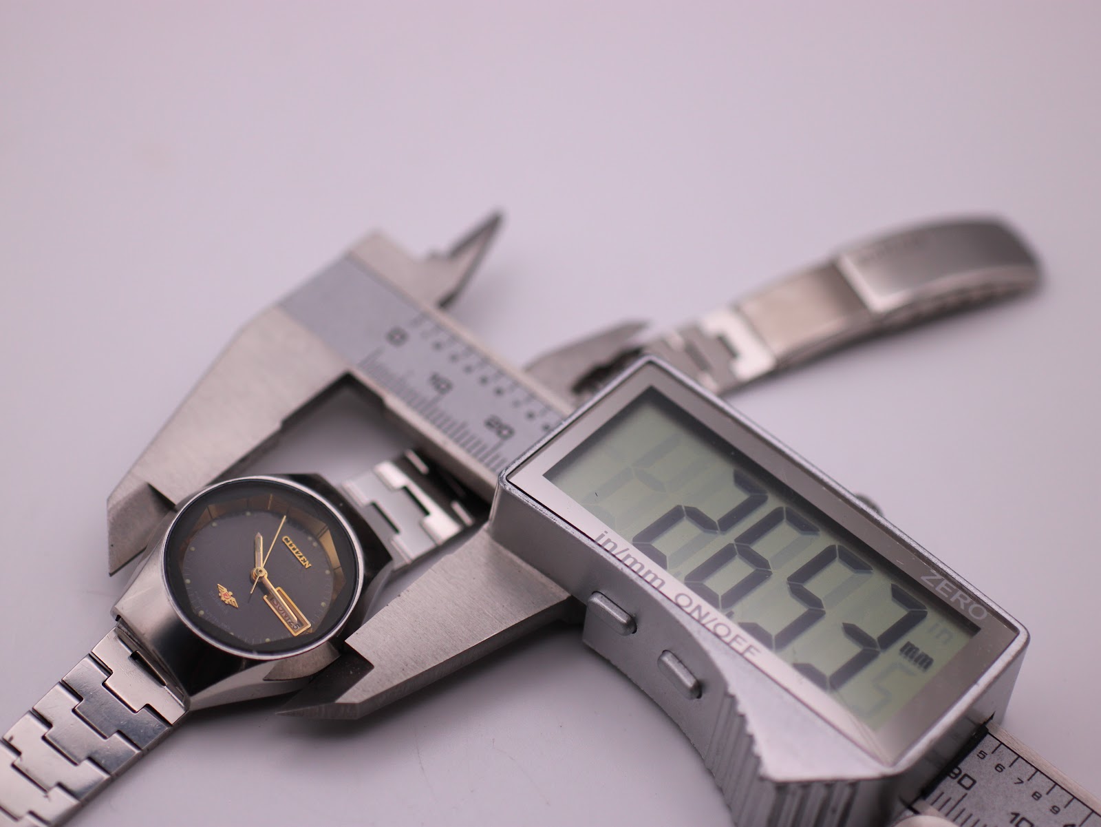 Digital caliper measuring the watch case diameter at 26.5mm, alongside the watch.