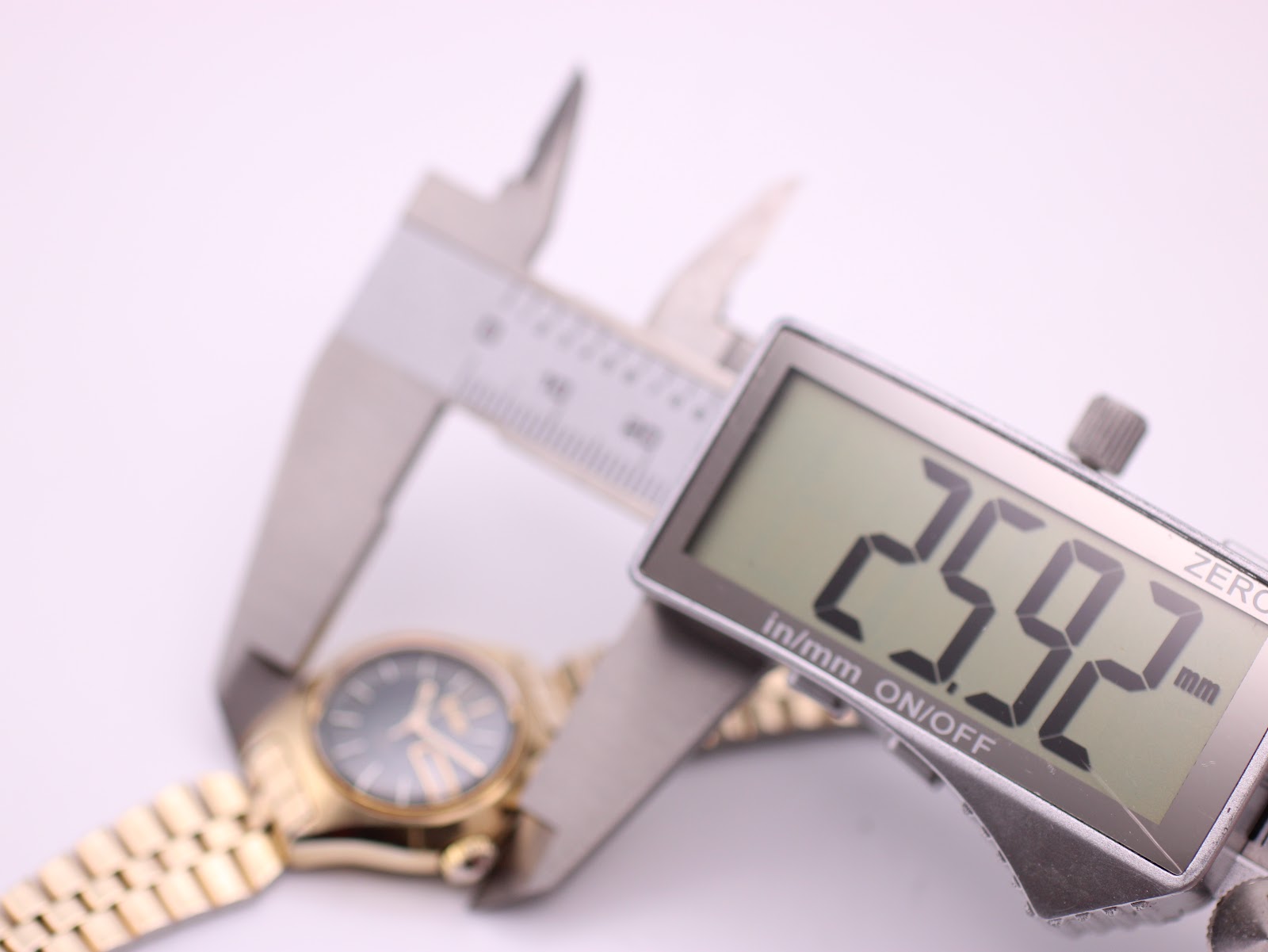 Digital caliper display showing the watch case diameter as 25.92mm, with the watch blurred in the background.
