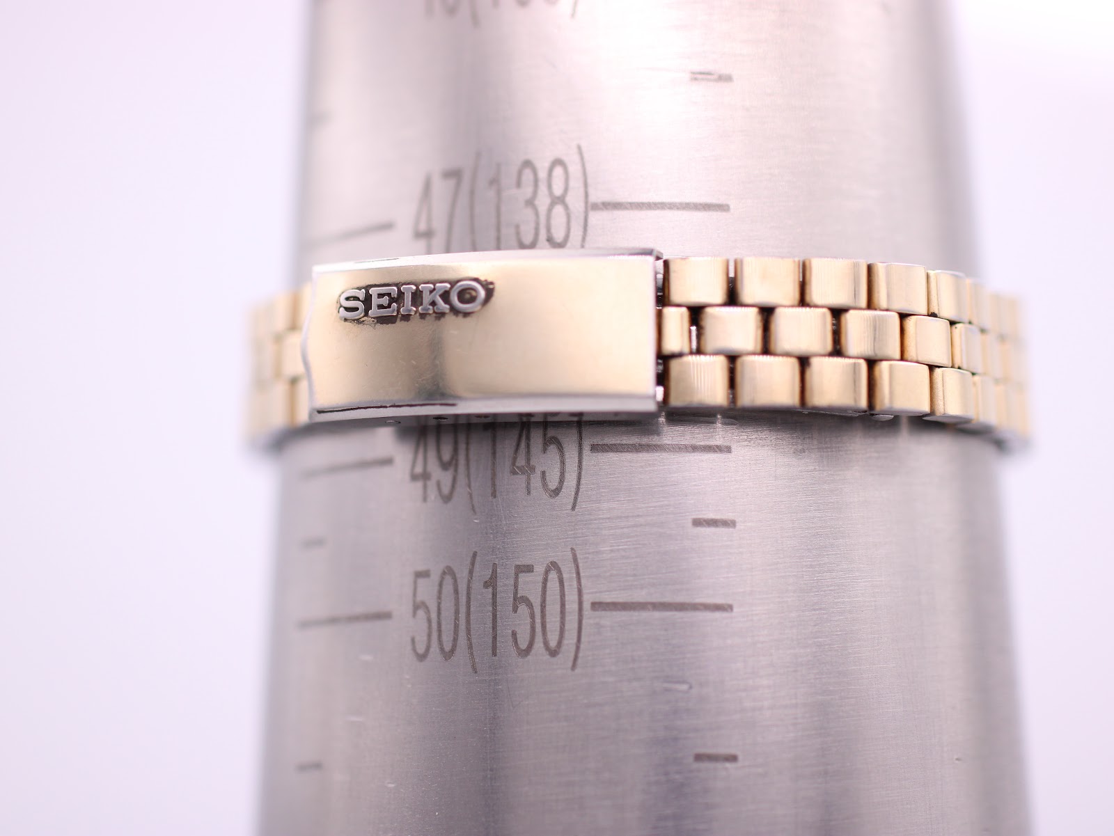 Close-up of the gold-toned Seiko bracelet on a wrist sizing gauge, showing a wrist circumference of 14.3cm.