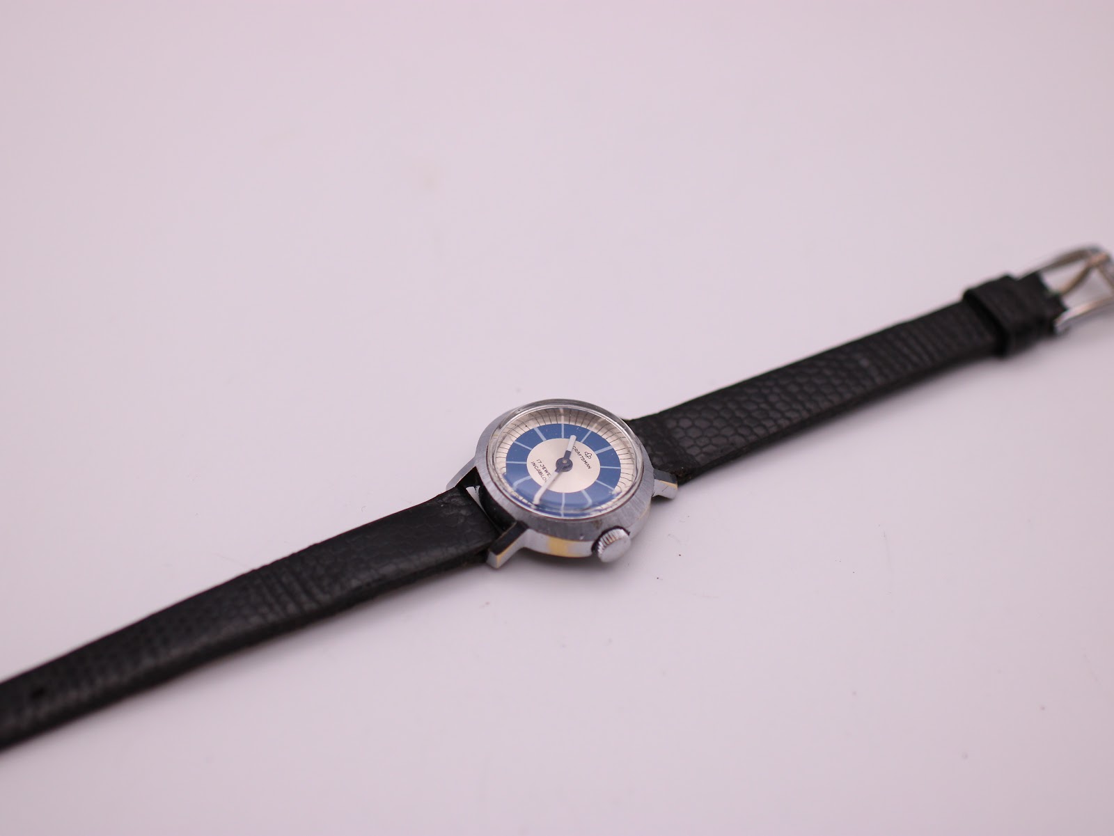 Top-down view of the Craftsman watch and its long black leather strap laid flat on a white surface.
