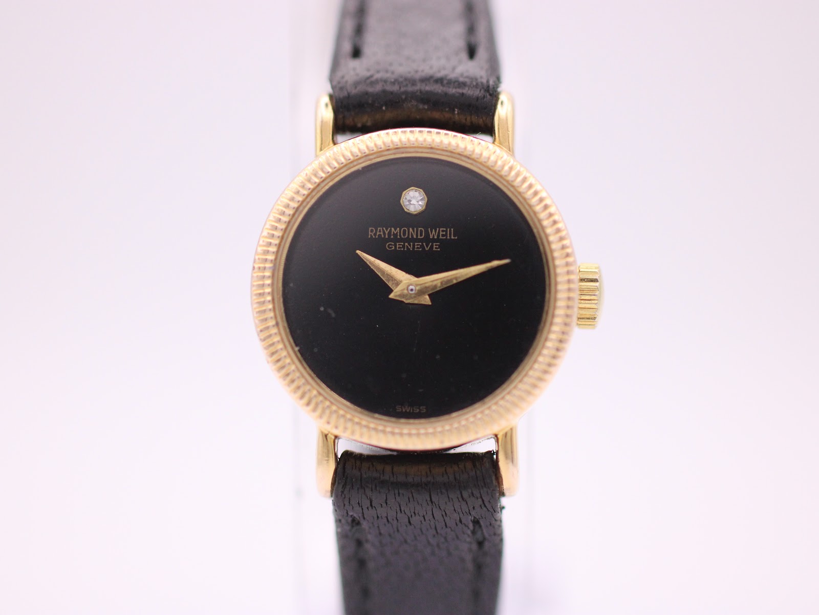 Front view of Raymond Weil 544 watch, gold tone case, black dial with diamond marker, on a black leather strap.