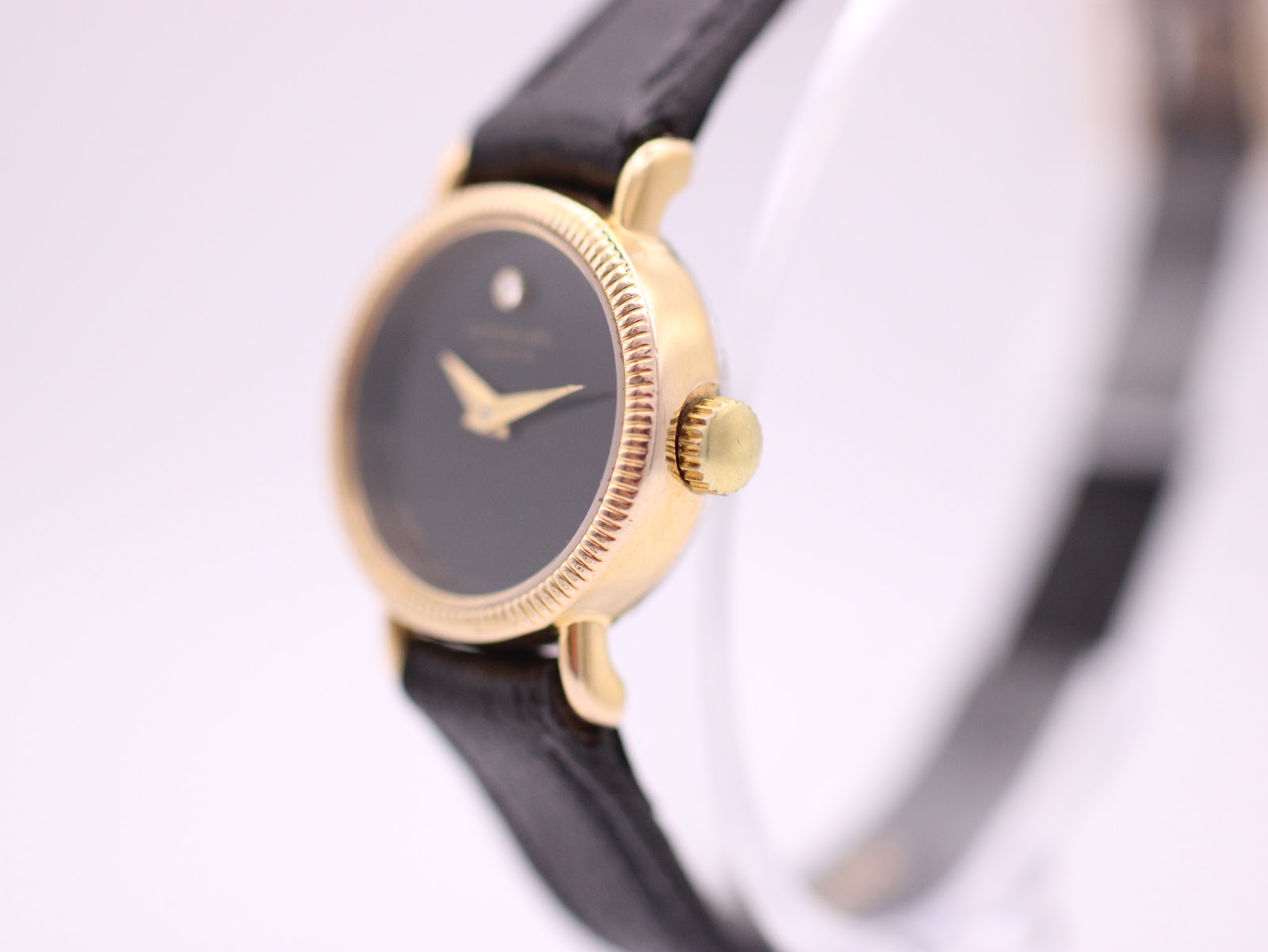 Angled close-up of Raymond Weil watch showing textured gold tone bezel and crown.