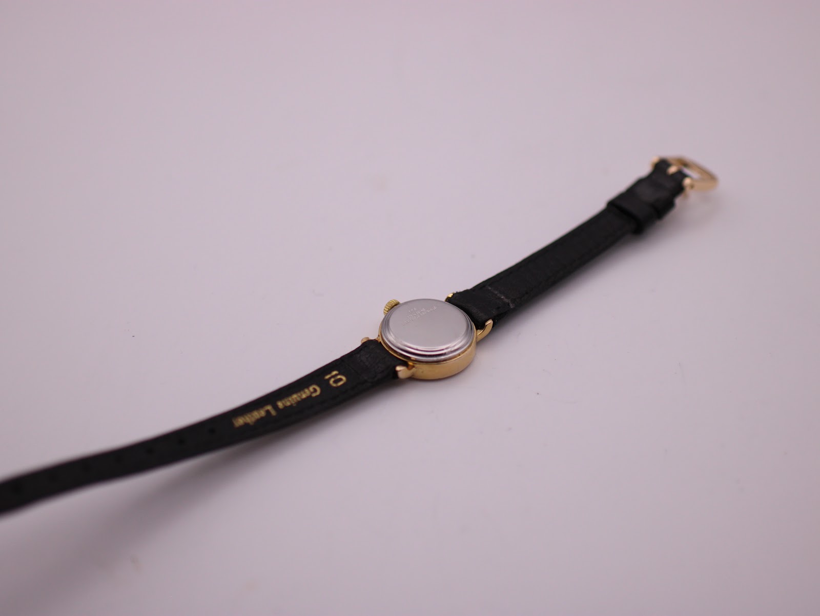 Rear view of the watch on its strap, showing the stainless steel case back and "Genuine Leather" on the strap.