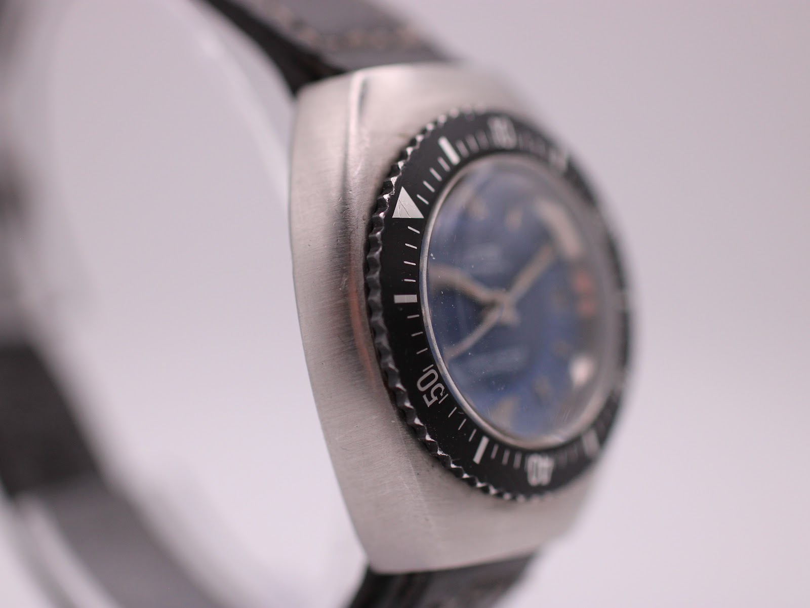 Close-up side view of the watch bezel and case, focusing on the marker at '10' and the brushed finish.