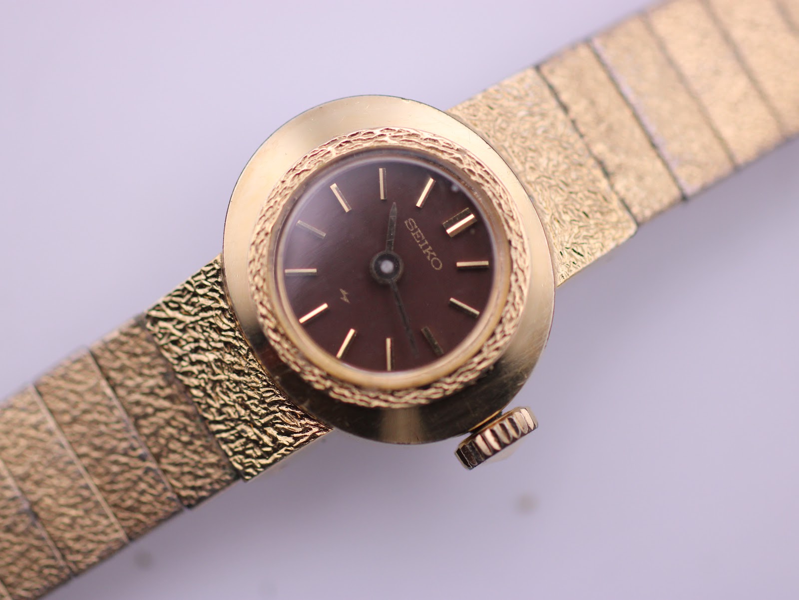 Close-up of the vintage Seiko's brown sunburst dial with gold hands and baton indices, framed by the textured gold bezel.