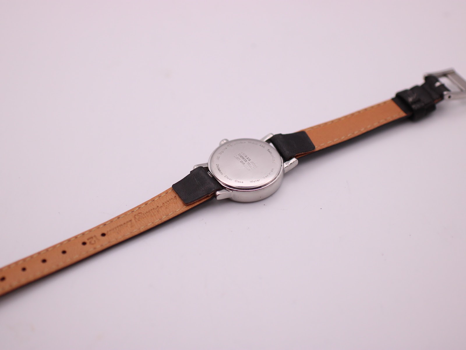Rear view of the Mondaine watch, showing the stainless steel case back and the light brown underside of the black leather strap.