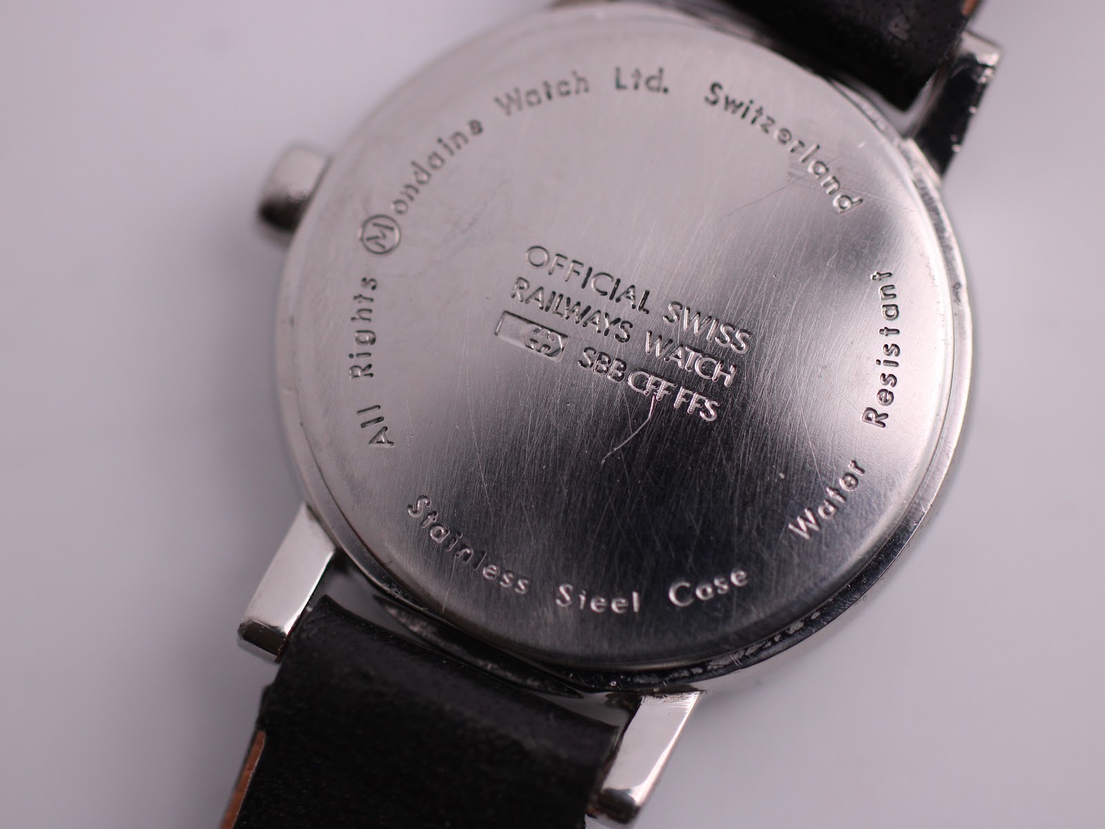 Detailed close-up of the stainless steel case back, showing 'MONDAINE Watch Ltd. Switzerland' and 'OFFICIAL SWISS RAILWAYS WATCH SBB CFF FFS' engravings, with some surface scratches.