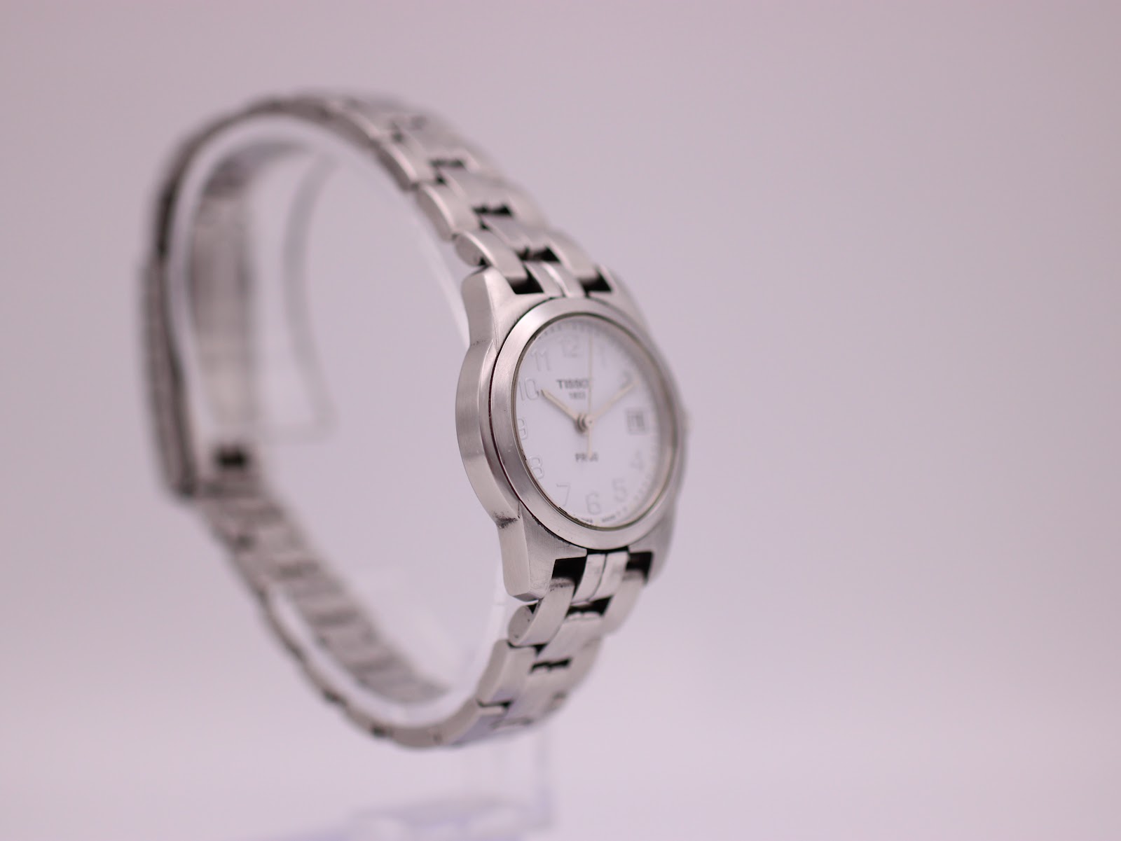 Angled side view of the Tissot PR 50 watch on a stand, highlighting the case profile and bracelet links.