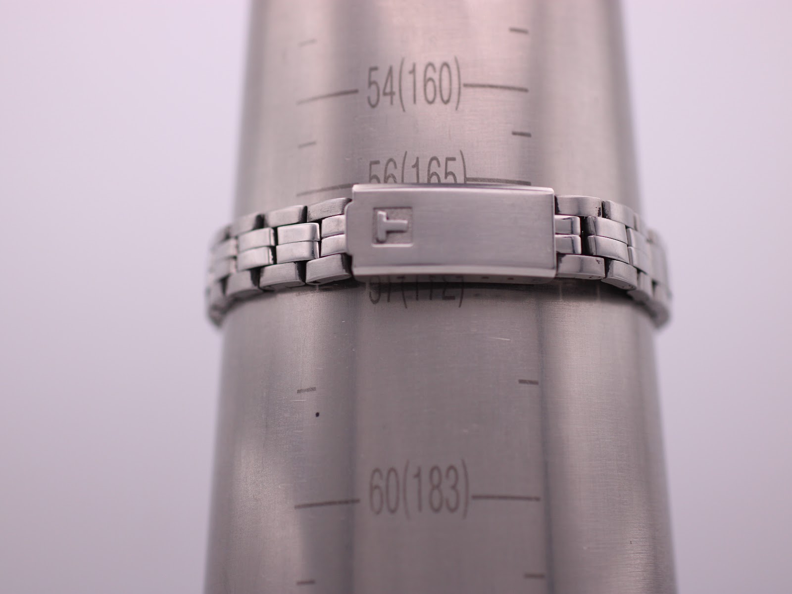 Close-up of the Tissot PR 50 stainless steel bracelet on a wrist sizing gauge, showing a circumference of approximately 16.5cm. The clasp has a signed Tissot 'T'.