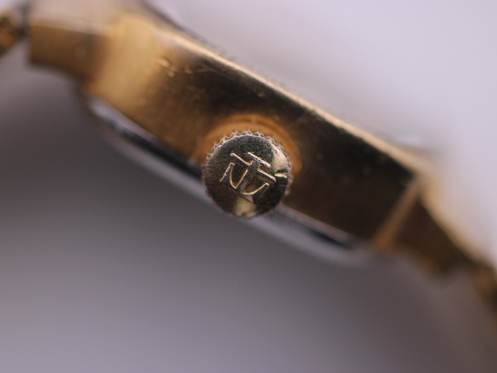 Extreme close-up of the Tissot Stylist crown, clearly showing the embossed Tissot 'T' logo.
