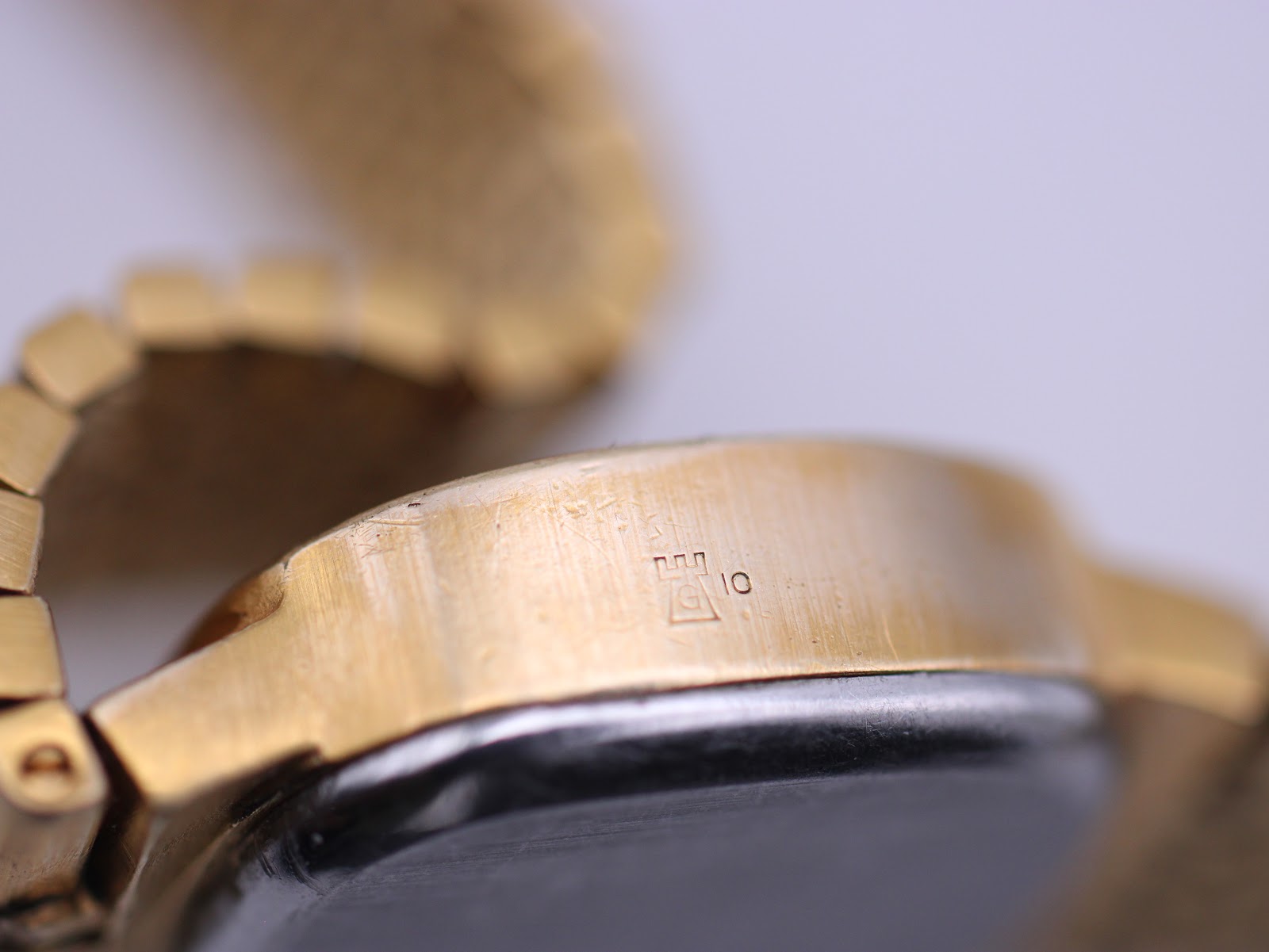 Close-up of the side of the Tissot Stylist case, showing the 'G 10 MICRONS' gold plating mark.