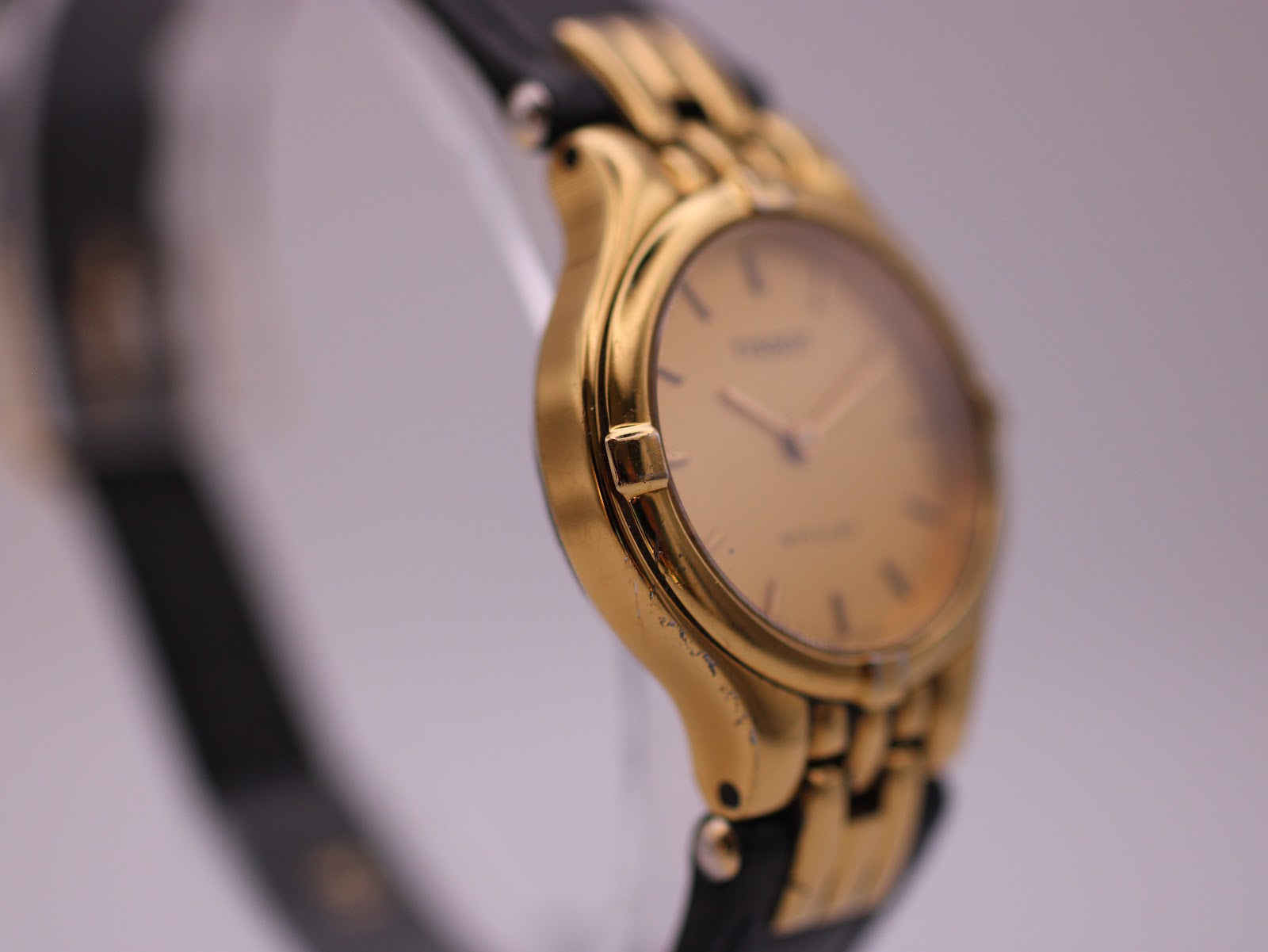 Angled side view of the watch, showing the gold-tone case, integrated lugs, and slight wear on the plating.