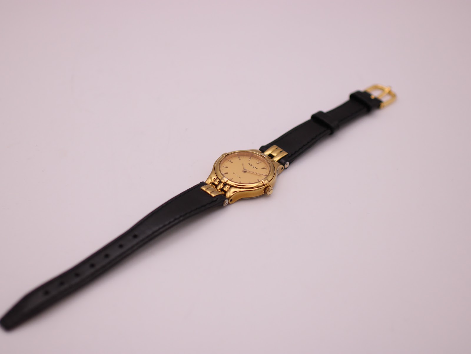 Overhead view of the entire watch, displaying the black leather strap and gold-tone buckle.