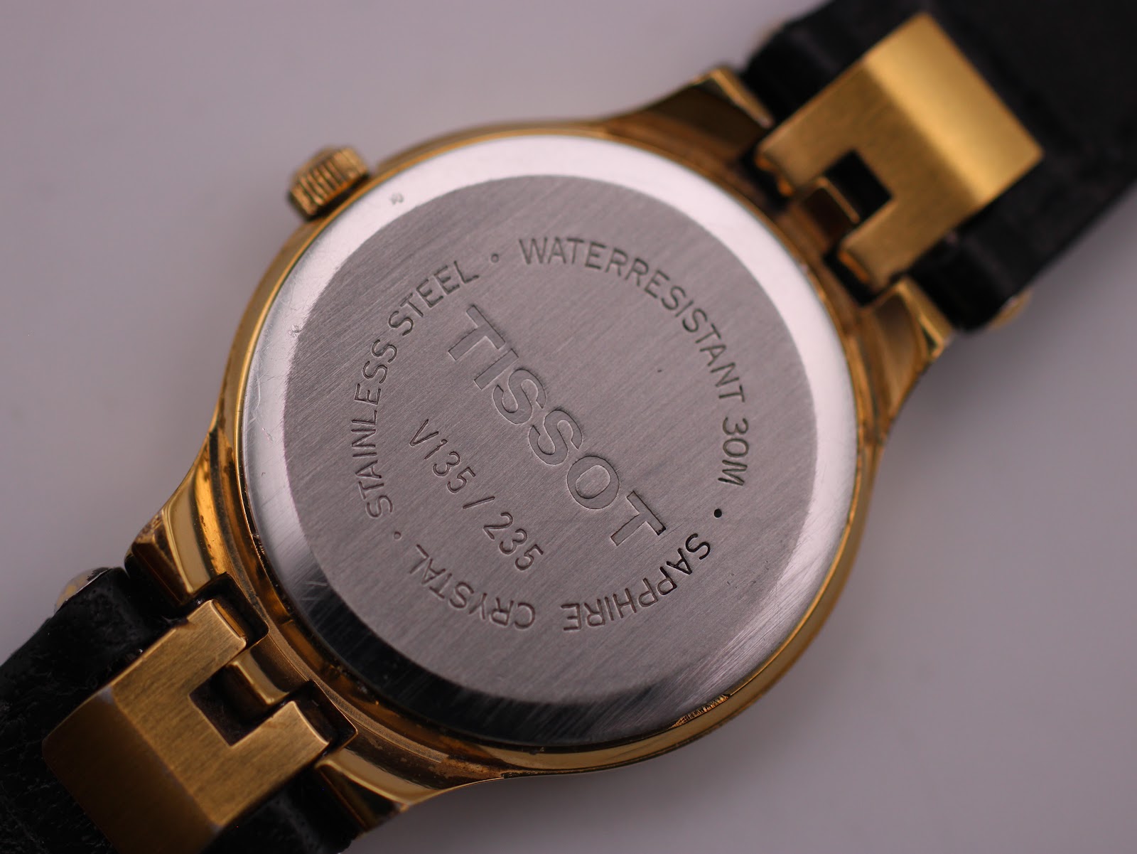 Detailed close-up of the stainless steel case back, showing 'TISSOT', 'WATERRESISTANT 30M', 'SAPPHIRE CRYSTAL', and model number V135/235.