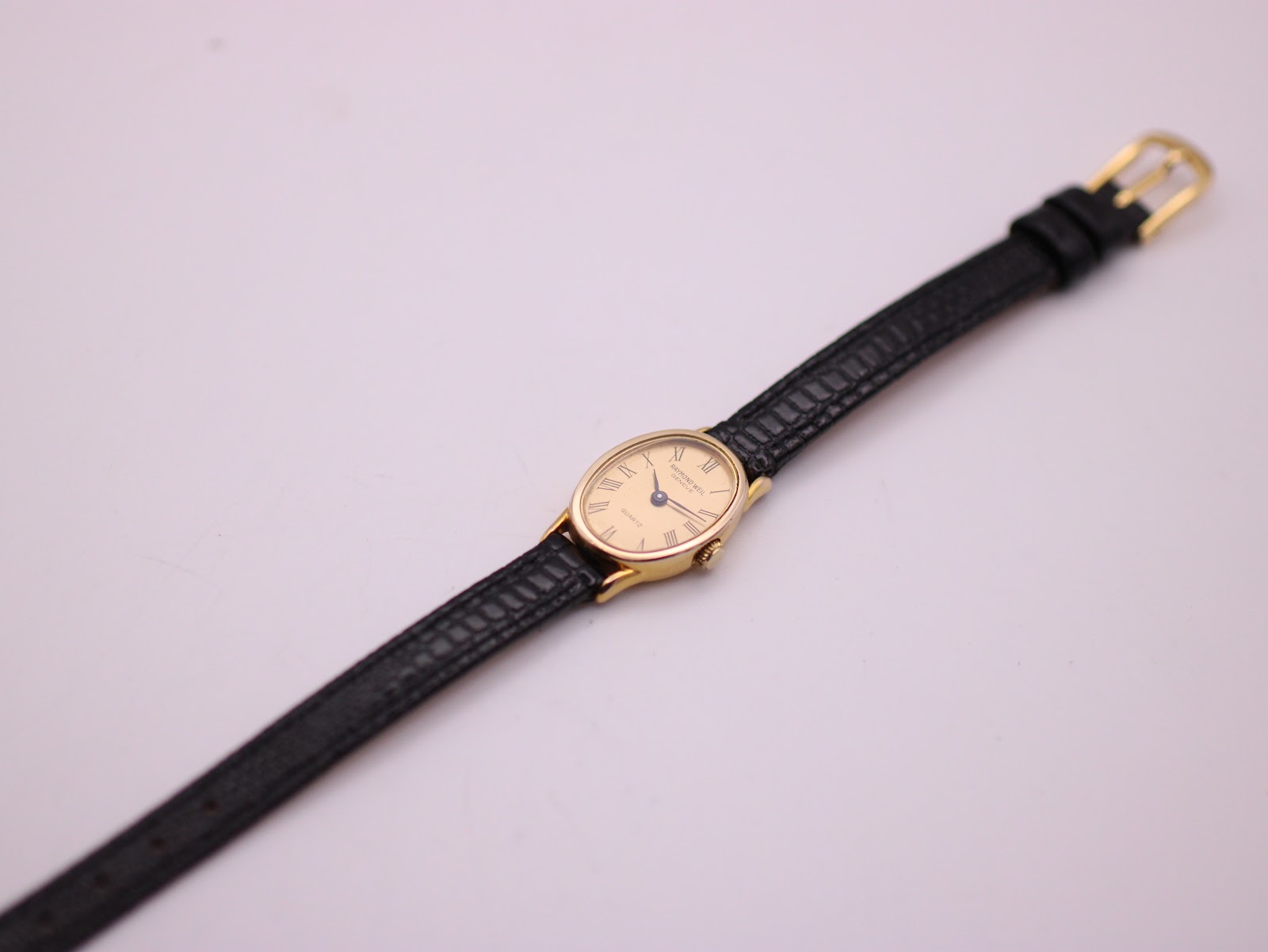 Top-down full view of the Raymond Weil 5712 watch with its black leather strap laid flat on a white surface.