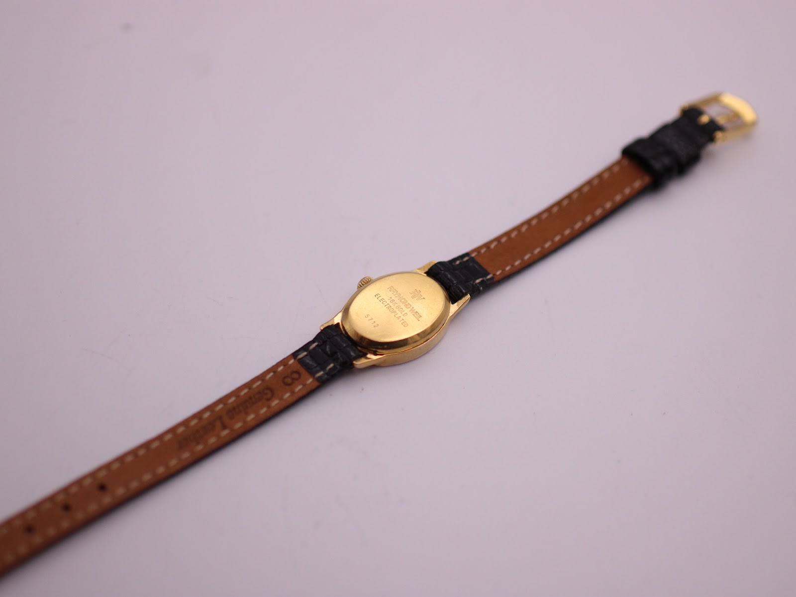 View of the watch from the back, showing the case back and the underside of the black leather strap with its brown lining.