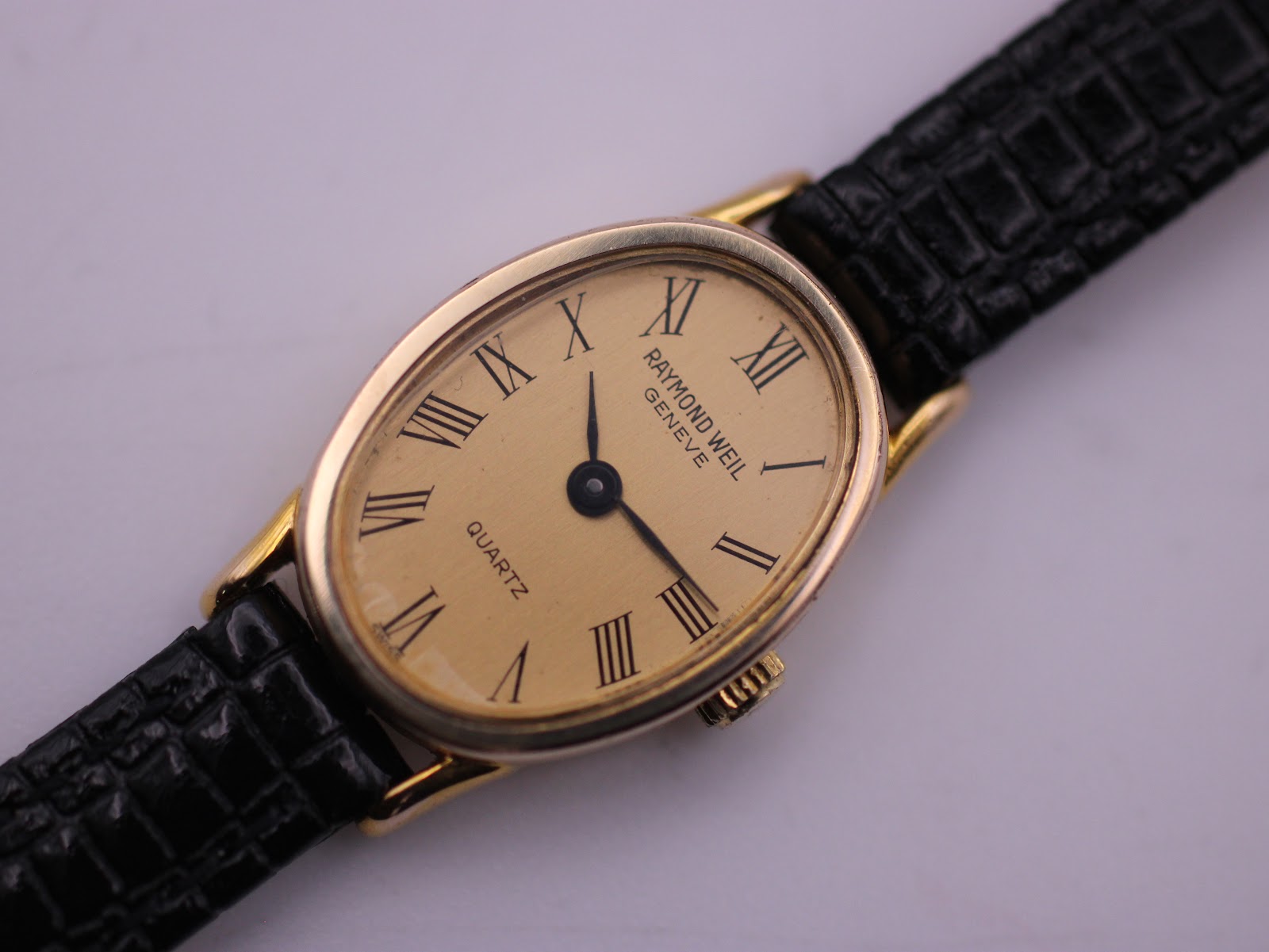 Close-up, slightly angled view of the Raymond Weil watch dial, showcasing the champagne face, Roman numerals, and gold-tone case details.