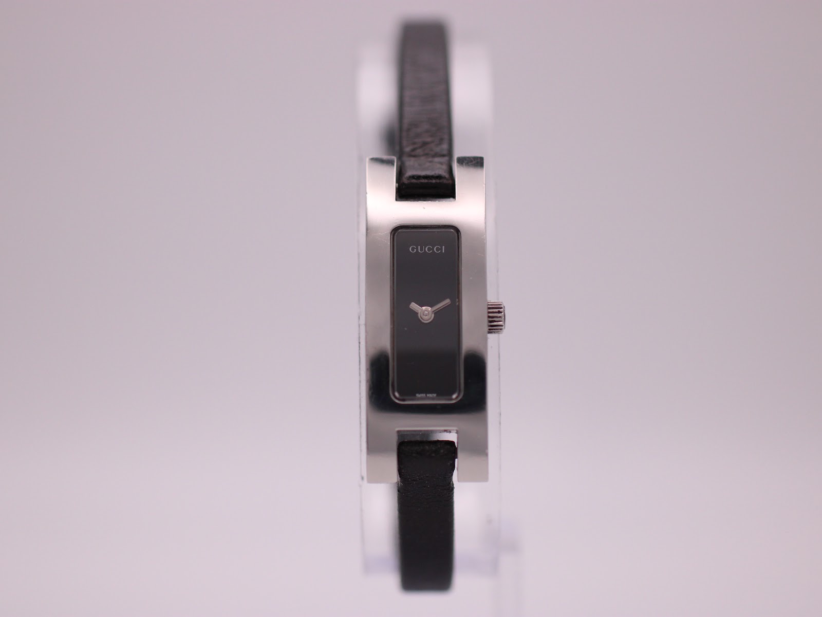 Front view of Gucci 3900L watch with rectangular silver-tone case, black minimalist dial, and black leather strap.