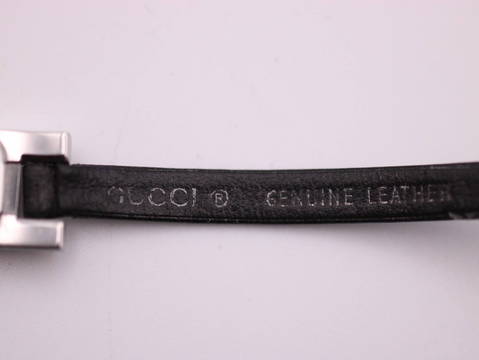 Close-up of the underside of the black leather strap, showing "GUCCI ® GENUINE LEATHER" embossed text.