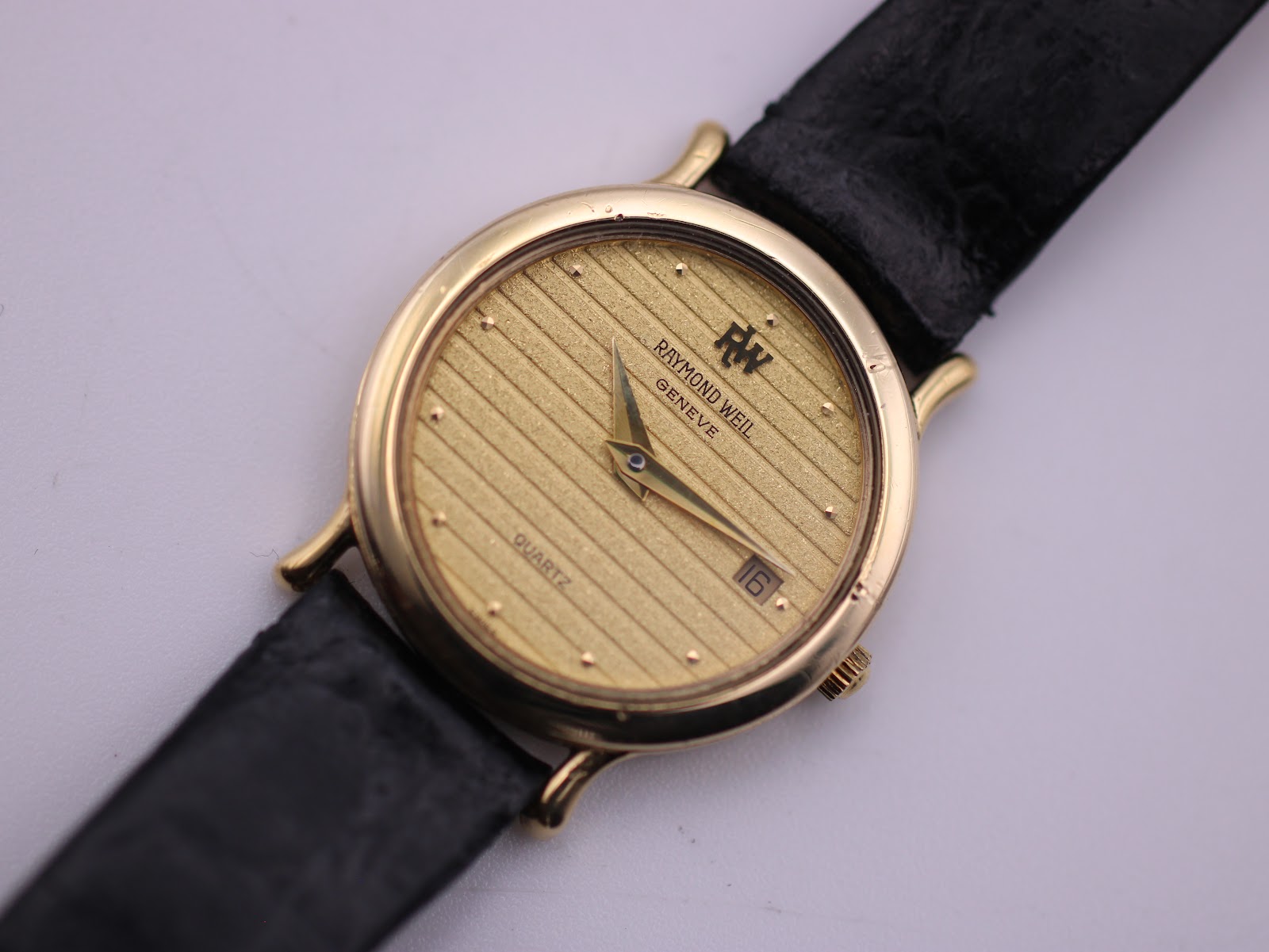 Close-up front view of the Raymond Weil gold dial with horizontal texture, applied baton markers, and date window at 3 o'clock.