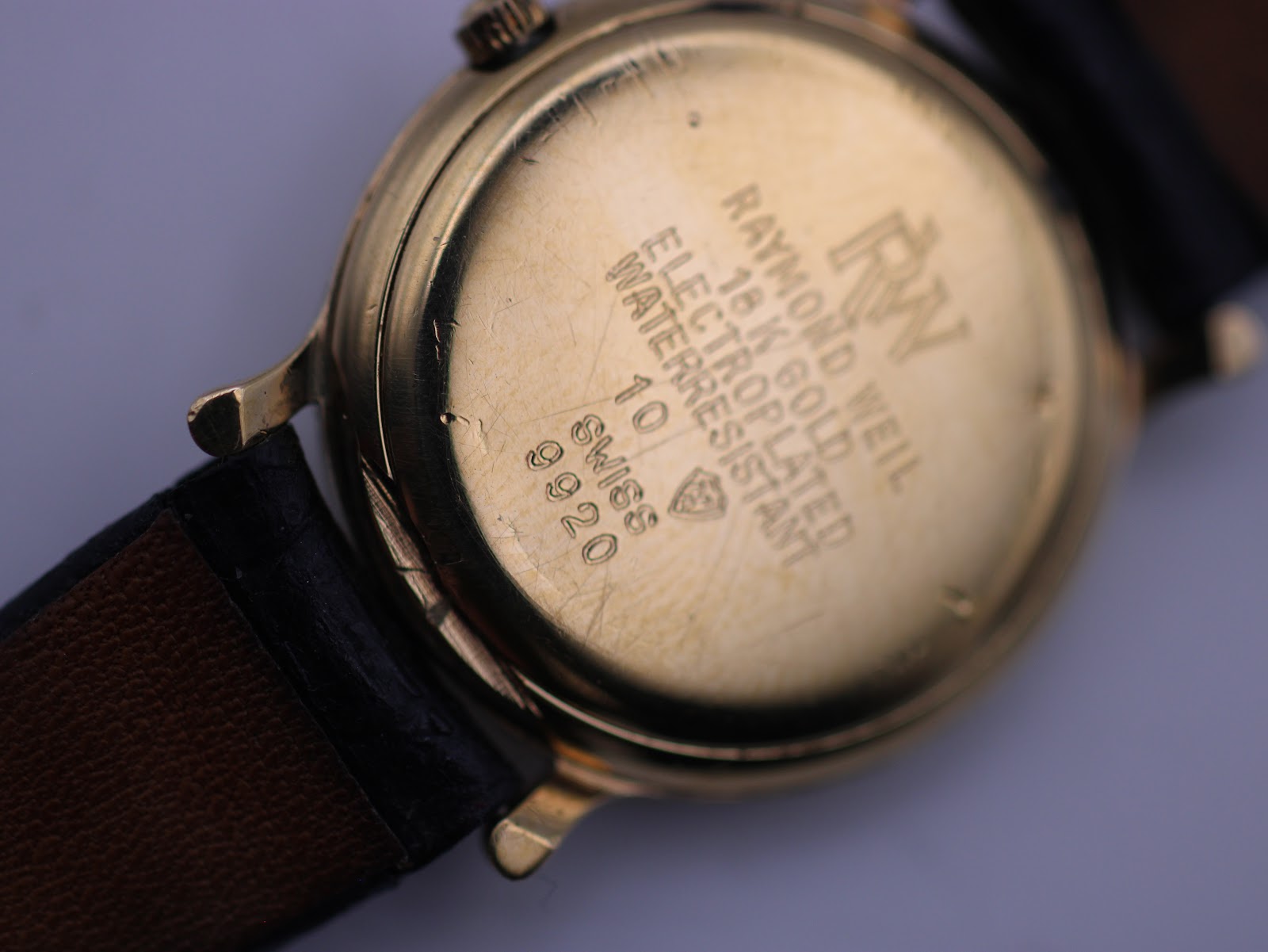 Close-up of the watch case back showing engravings: 'RAYMOND WEIL', '18 K GOLD ELECTROPLATED', 'WATERRESISTANT', 'SWISS', and model '9920'.