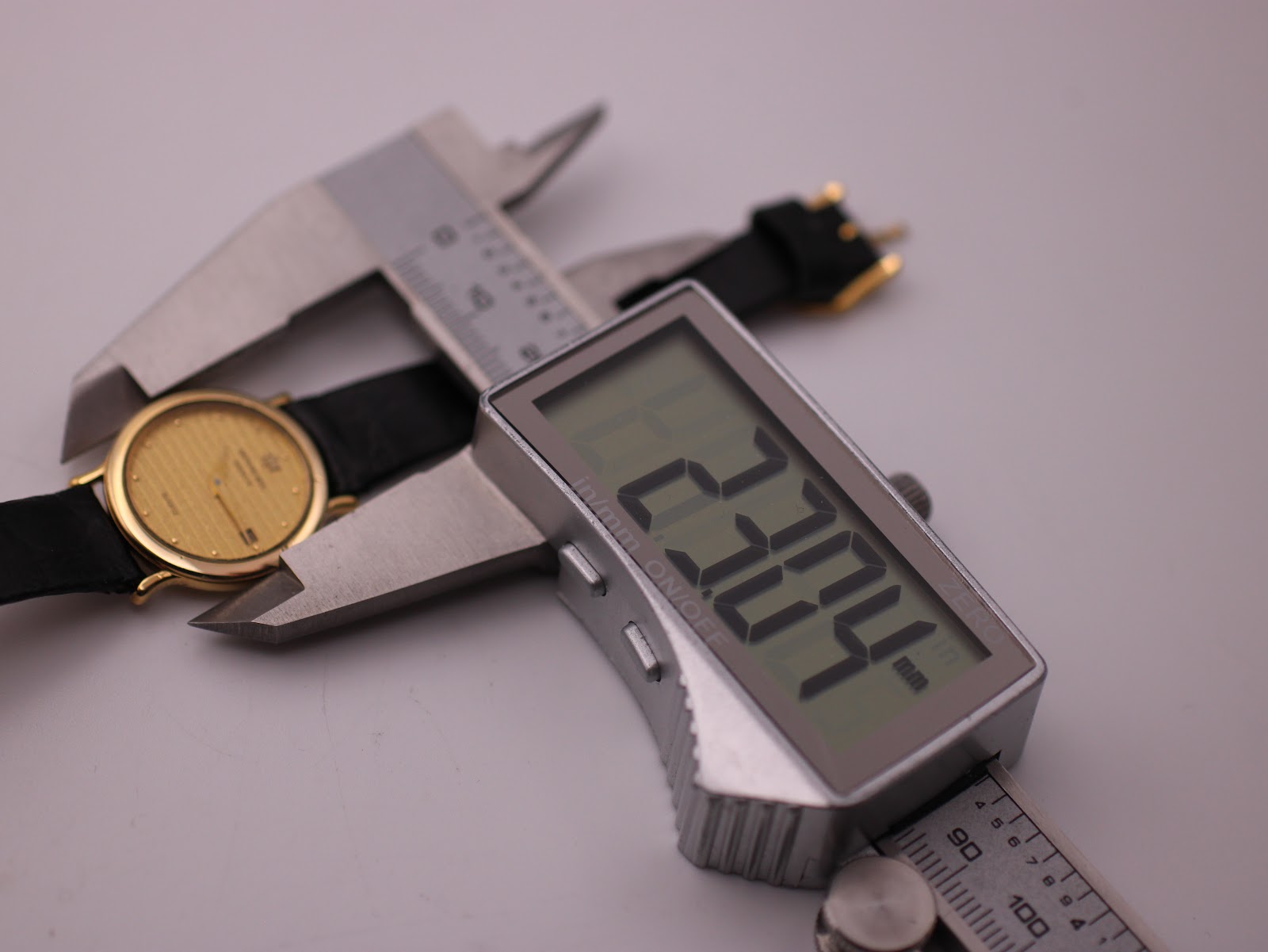 Digital caliper measuring the watch case diameter, displaying an exact measurement of 23.04mm.