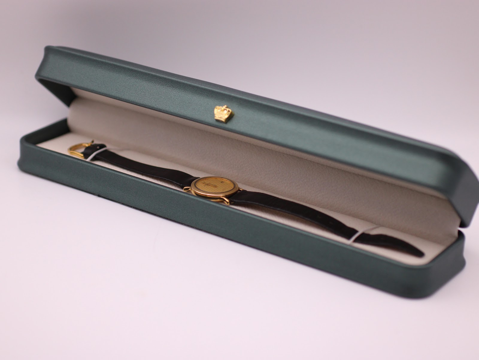 The Raymond Weil watch with black strap displayed open in a green presentation box with a gold crown emblem.