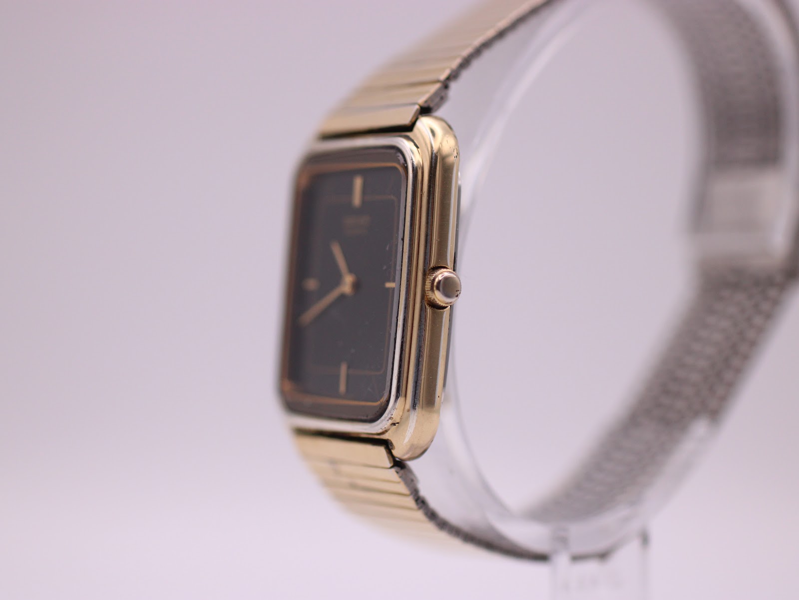 Side profile of the Seiko watch showing the gold-tone case, crown, and mesh bracelet on a display stand.