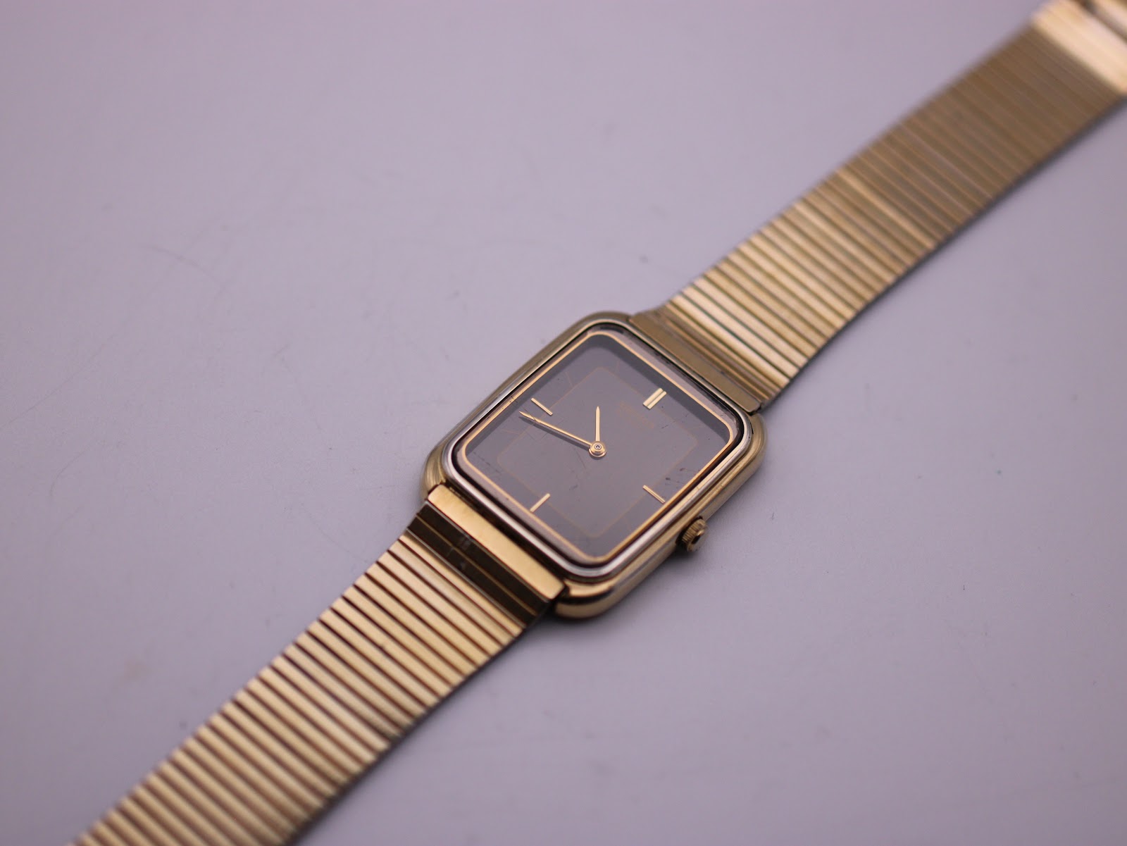 Overhead shot of the gold-tone Seiko watch with its mesh bracelet laid flat on a grey surface.