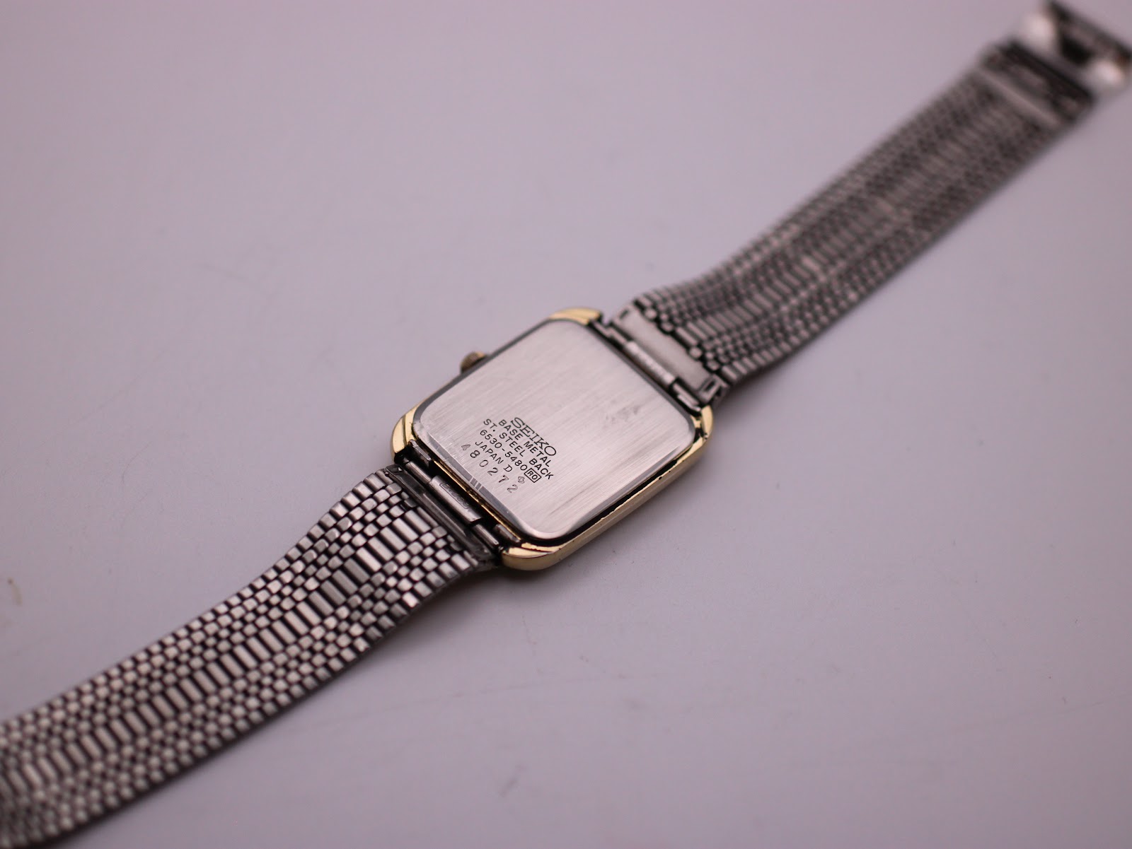 Angled rear view showing the stainless steel case back with engravings and the underside of the mesh bracelet.