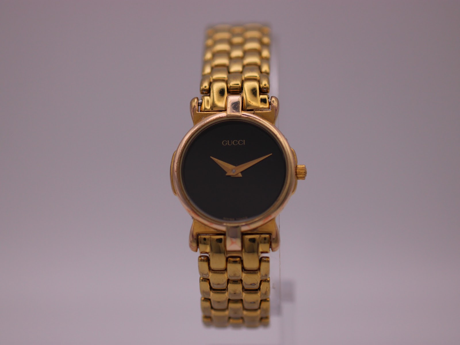 Front view of the vintage Gucci 3400 L watch with a gold-tone case and bracelet, featuring a black dial and gold hands.