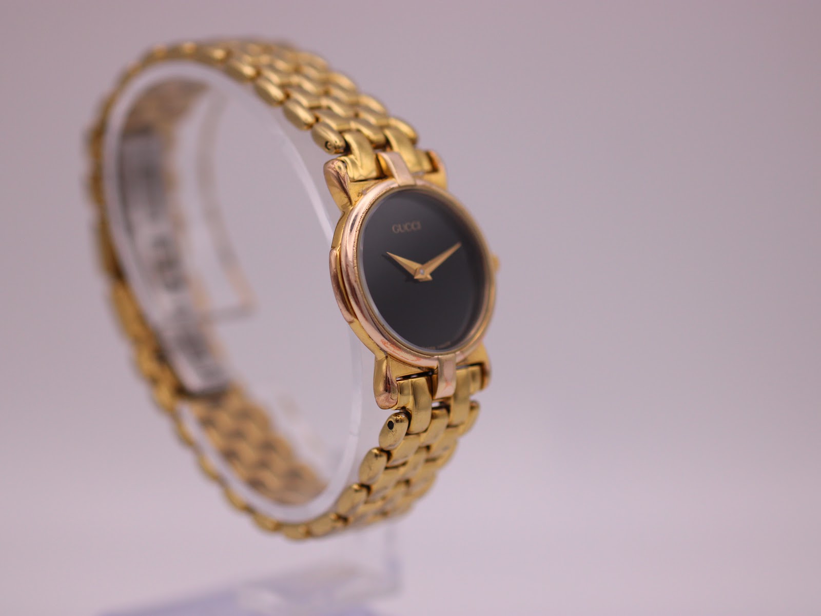 Angled right view of the Gucci 3400 L watch on a clear display stand, showing the clean black dial and integrated bracelet.