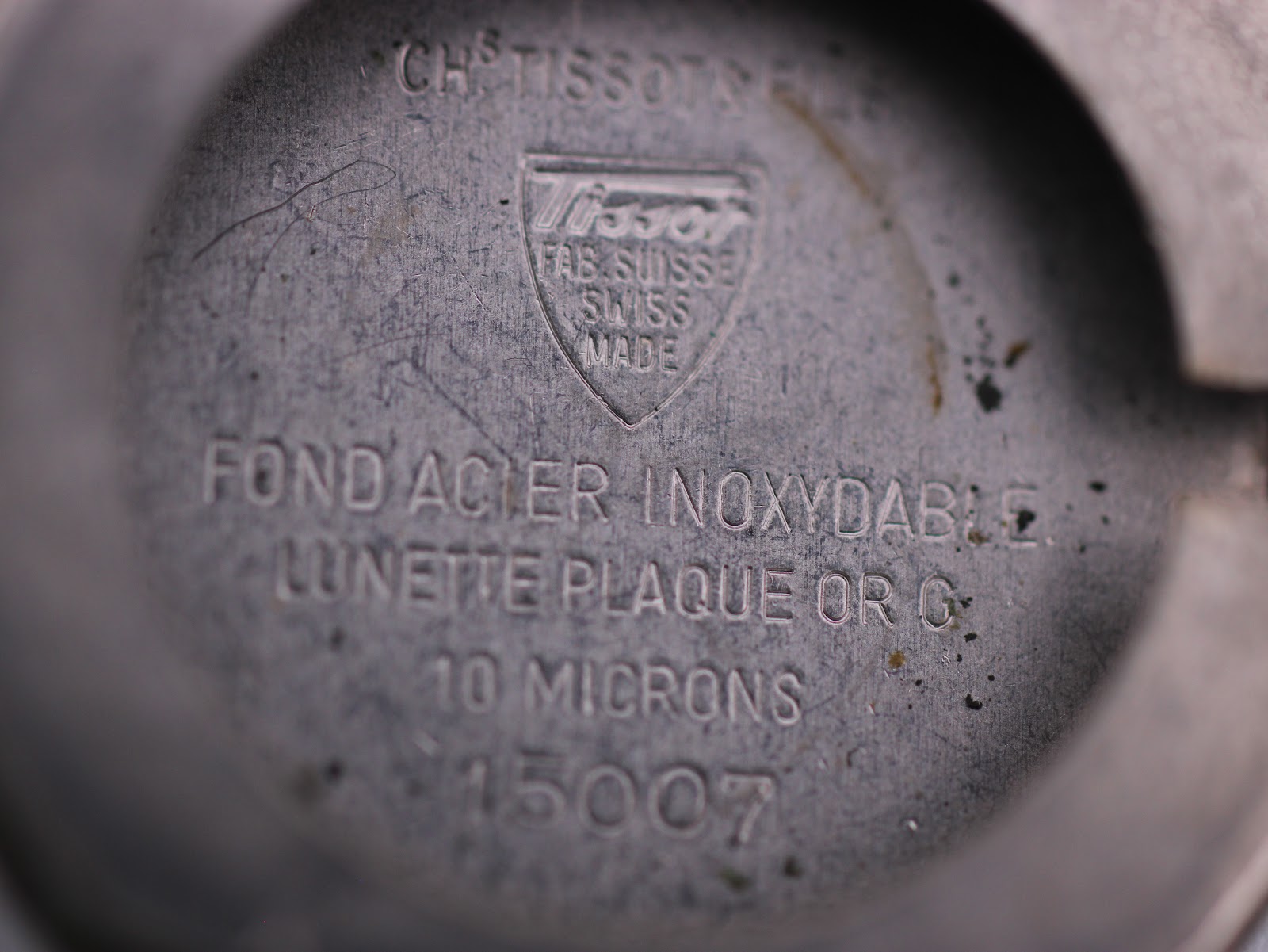 Close-up of the inner case back engraving, showing Tissot logo, "Fond Acier Inoxydable", "Lunette Plaque Or G 10 Microns" and serial number 15007.