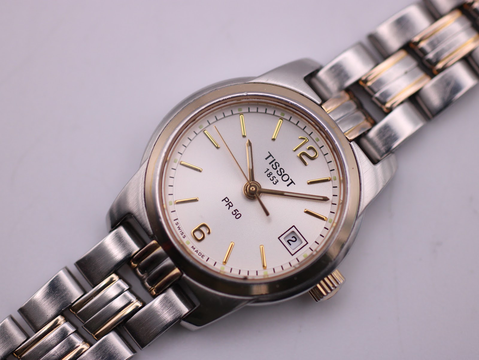 Close-up of the cream dial with gold-tone Arabic numerals, baton indices, hands, and date window.