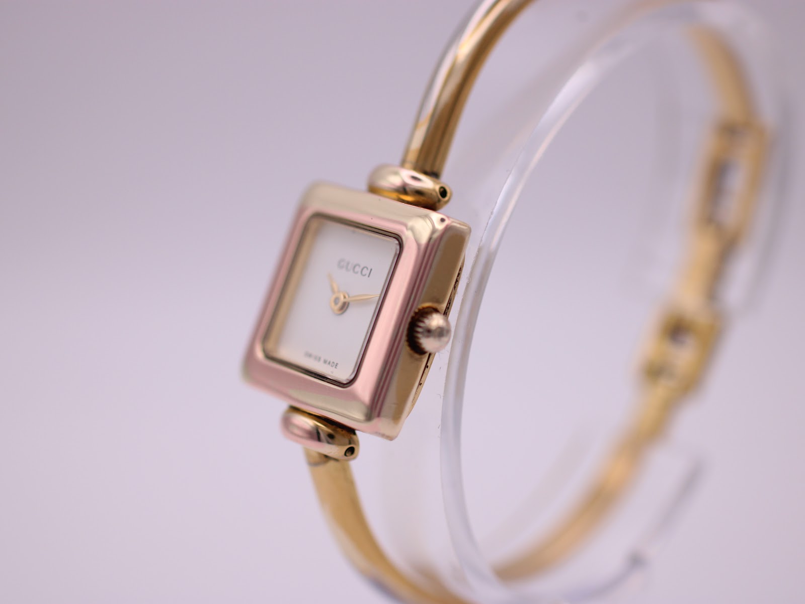 Angled side view of the Gucci 1900L watch, showing the gold-tone case, cream dial, crown, and integrated bangle bracelet design.