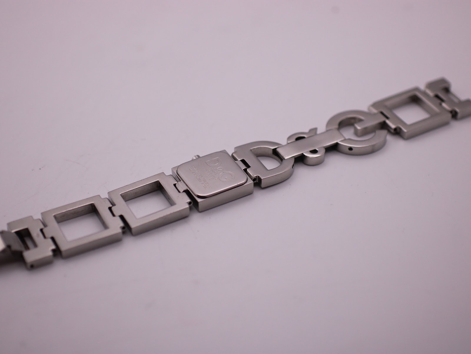 Angled overhead rear view of the D&G Time watch, showing the case back and the integrated stainless steel bracelet with square links and large D&G lettering.