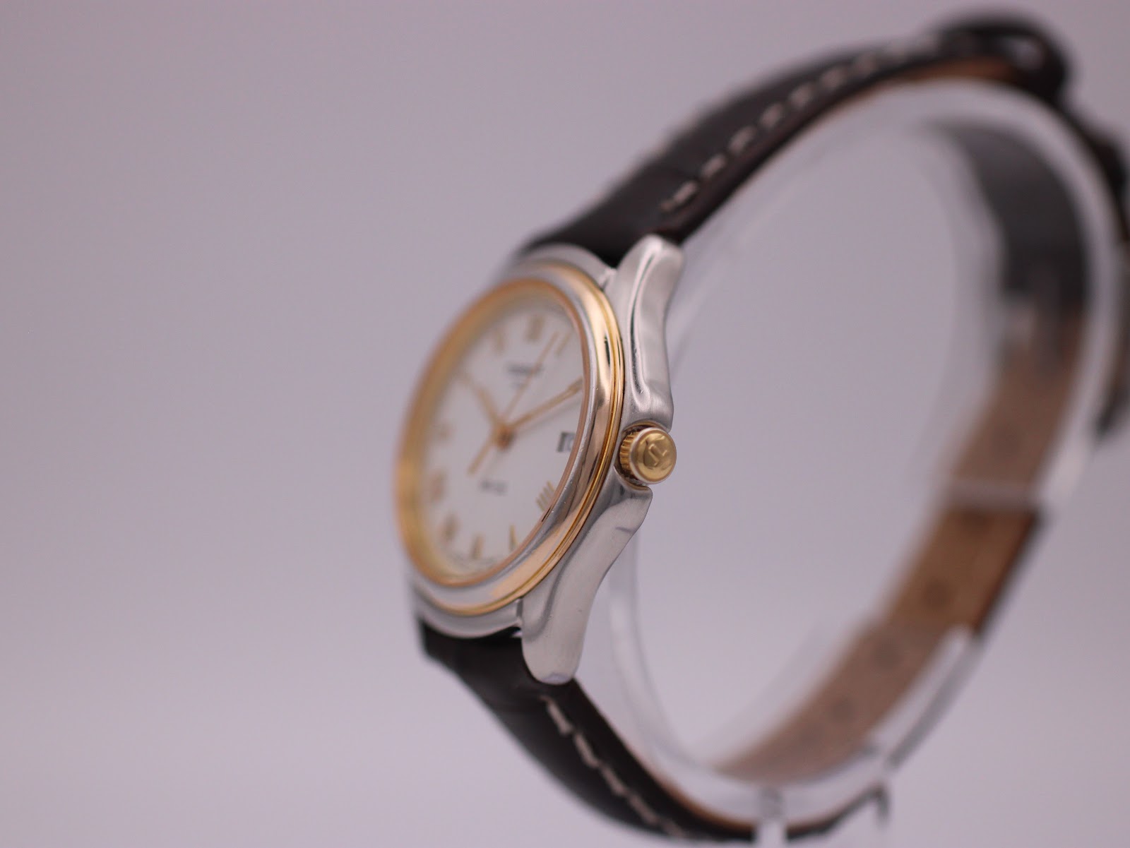 Right side view of the Tissot PR 50 watch on a display stand, highlighting the gold-tone crown and bezel.