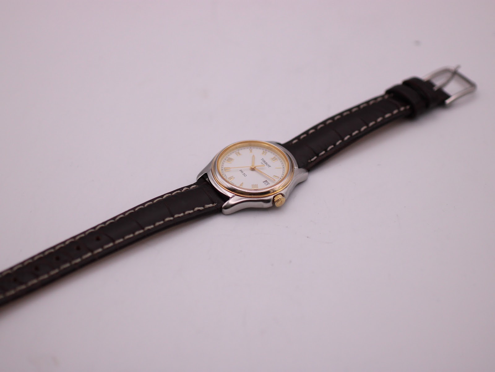 Overhead shot of the Tissot PR 50 watch with its brown leather strap extended flat against a white background.