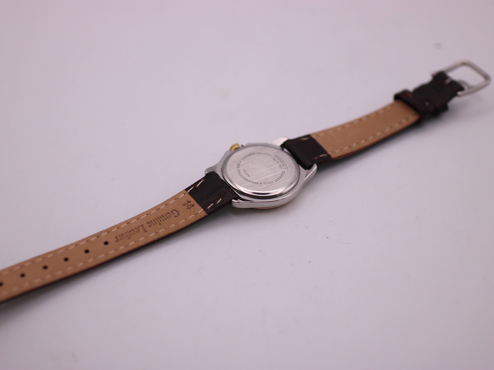 Rear view of the Tissot PR 50 watch laid flat, displaying the stainless steel case back and the 'Genuine Leather' stamp on the strap's interior.