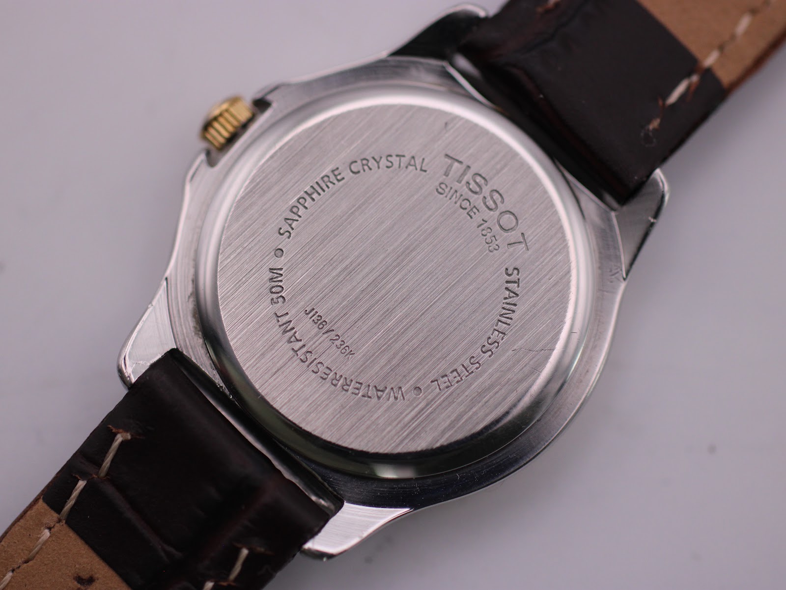 Detailed close-up of the Tissot PR 50's stainless steel case back, showing engravings for 'Sapphire Crystal', 'Water Resistant 50M', 'Stainless Steel', 'Tissot Since 1853', and serial number J186/236K.
