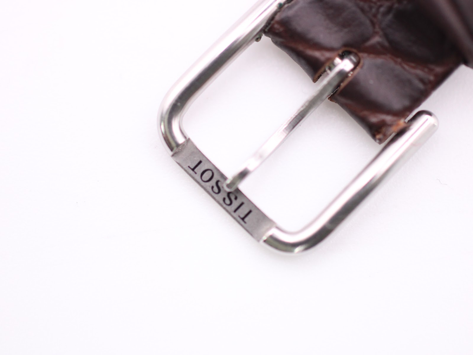 Close-up of the stainless steel pin buckle of the brown leather strap, clearly showing the 'TISSOT' engraving.