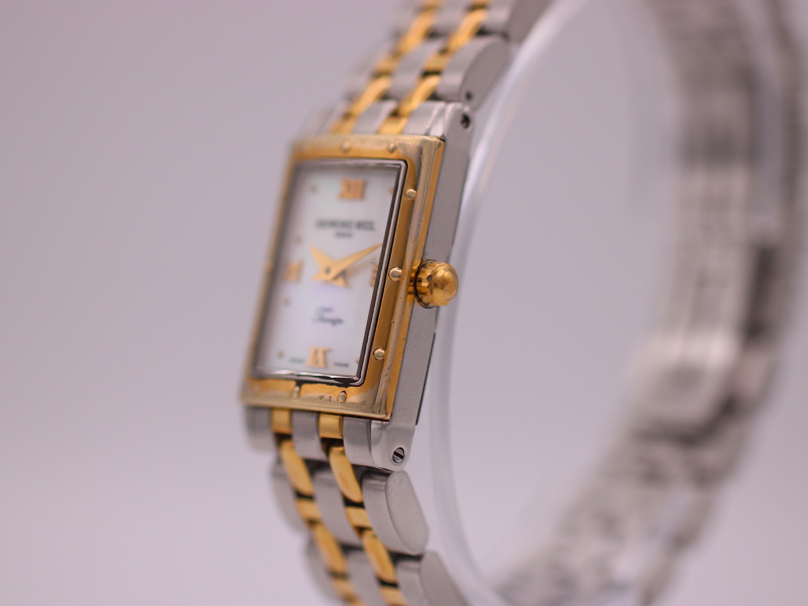 Angled side view of the Raymond Weil Tango watch, highlighting the gold-plated rectangular case and crown.