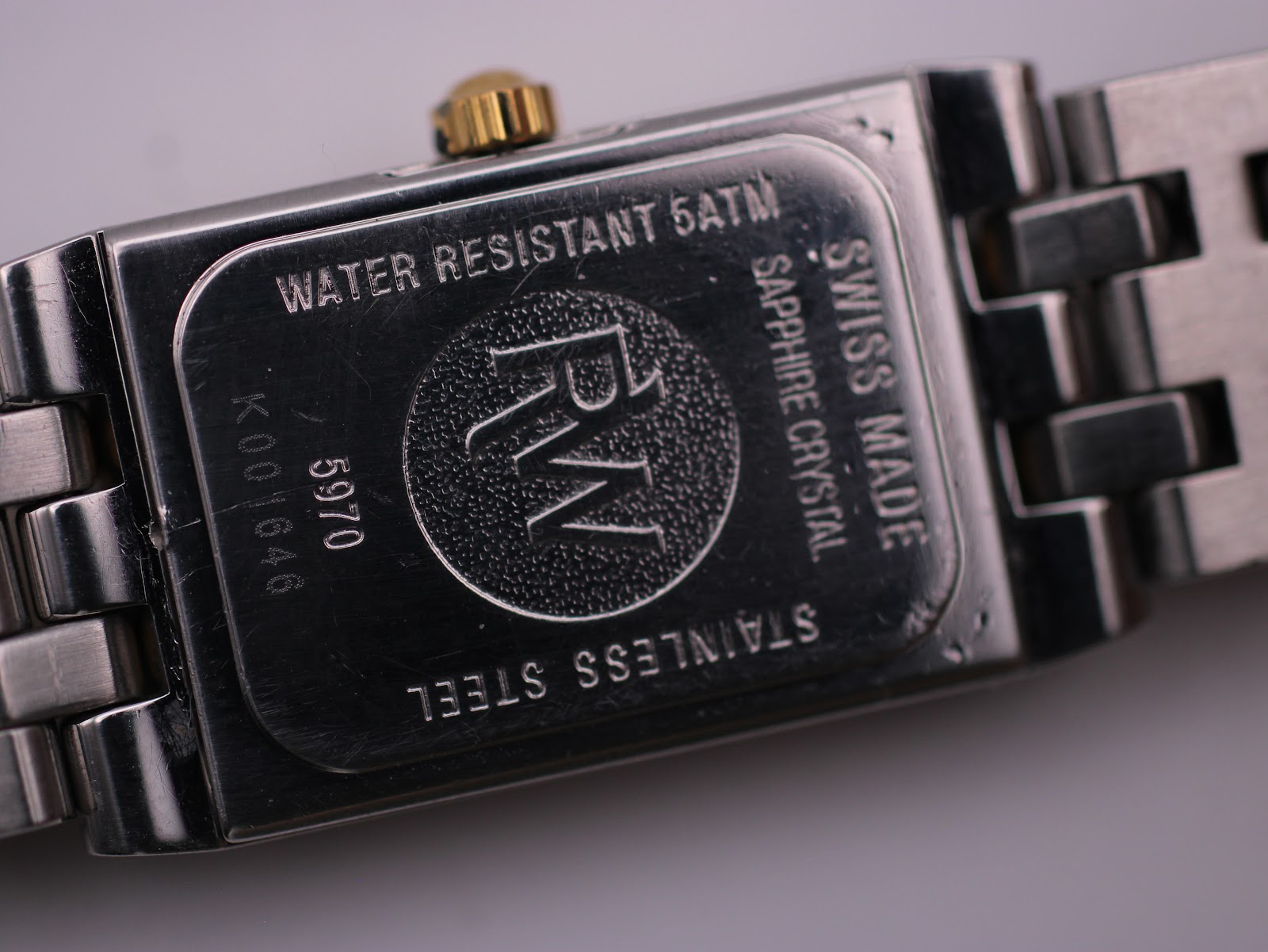 Close-up of the watch's stainless steel case back, detailing 'Water Resistant 5ATM', 'Swiss Made', 'Sapphire Crystal', serial 'K001646', and model '5970'.