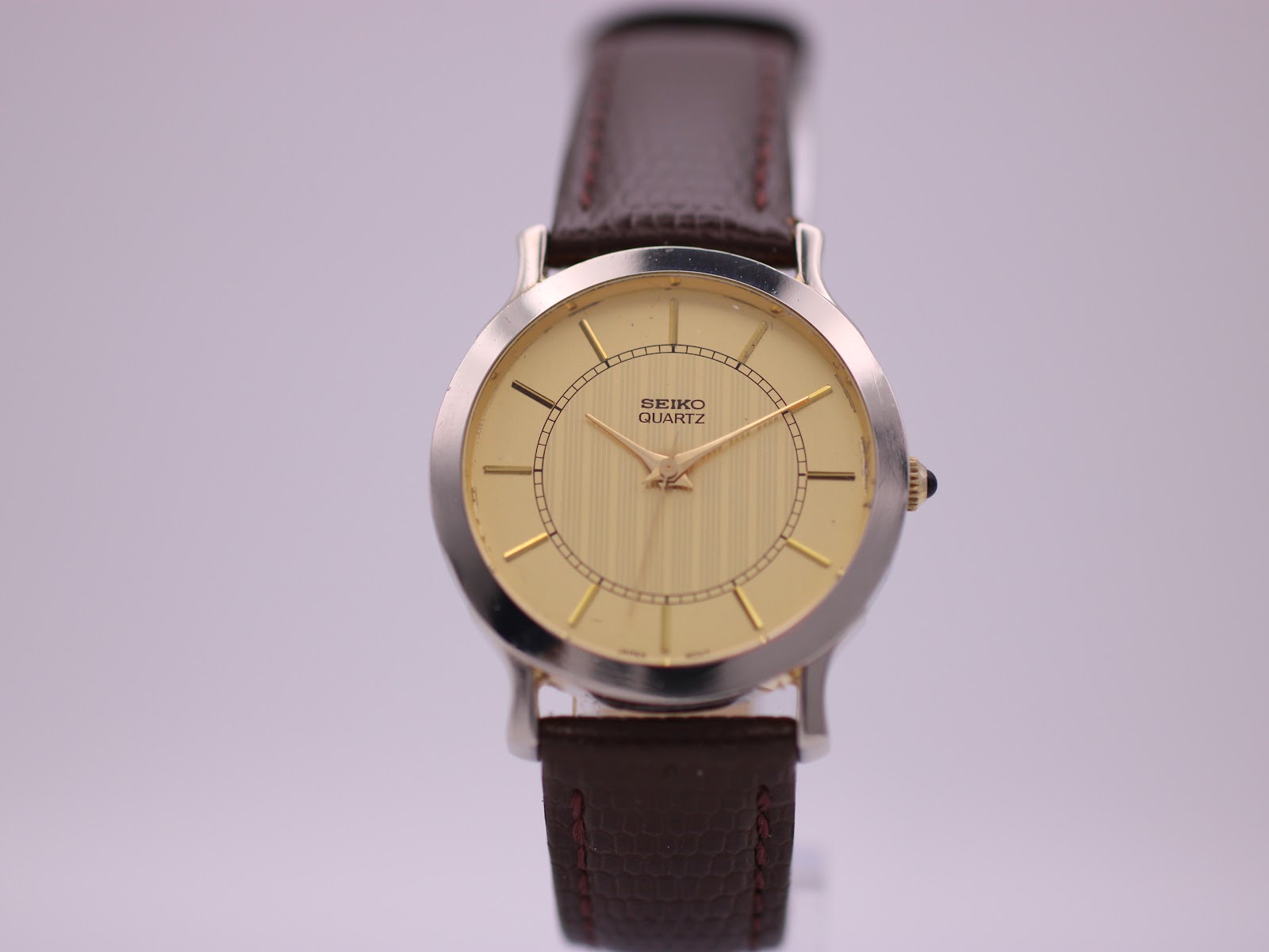 Front view of the Seiko V701-0070 watch with champagne dial and brown leather strap on a light background.