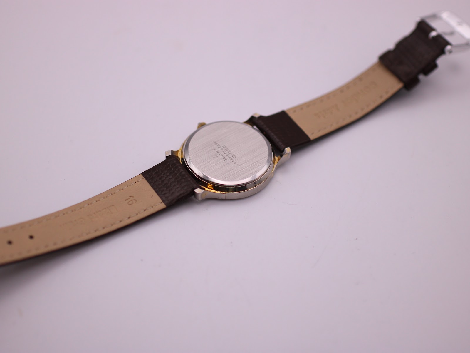 View of the brushed stainless steel case back and the lighter coloured underside of the brown leather strap, showing '16' printed near the lug.