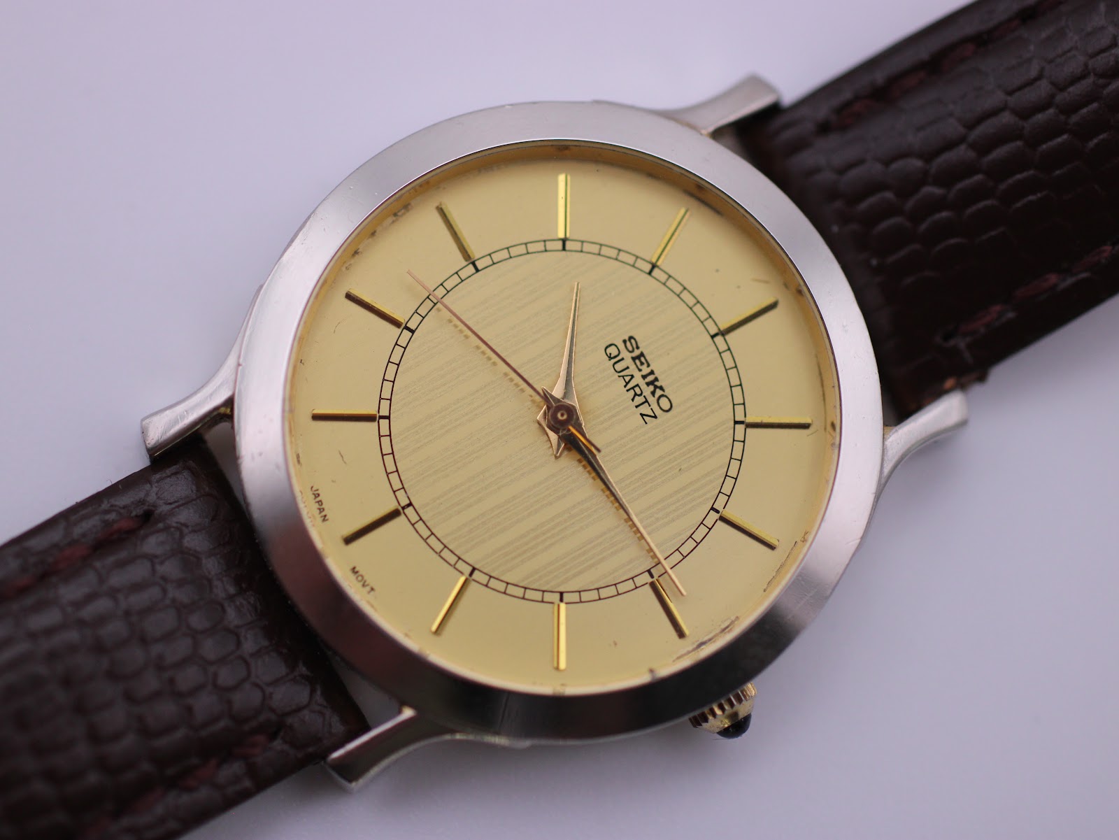 Close-up of the champagne dial with vertical stripe texture, gold-tone baton indices, and 'SEIKO QUARTZ' branding.