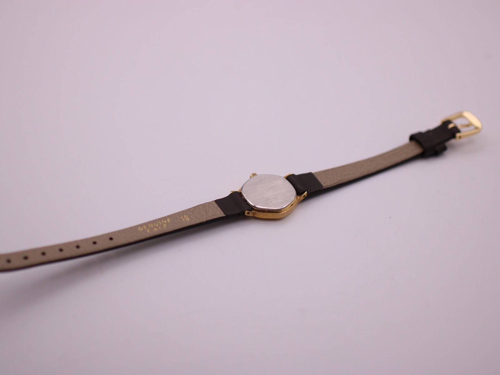 View of the watch case back and the underside of the brown leather strap, showing 'GENUINE LEATHER 10'.