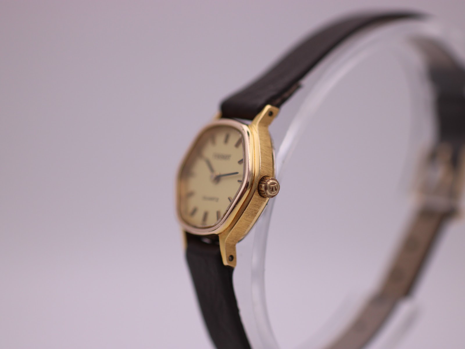 Angled side view of the Tissot watch, showing the brushed gold-coloured case and the unsigned crown.