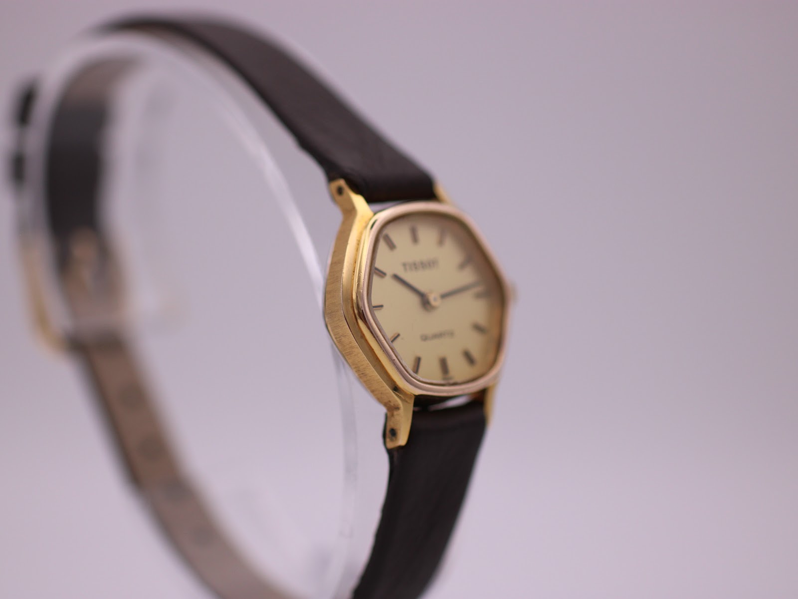 Overhead angled view of the Tissot watch on a clear stand, highlighting the cream dial and the brown strap.