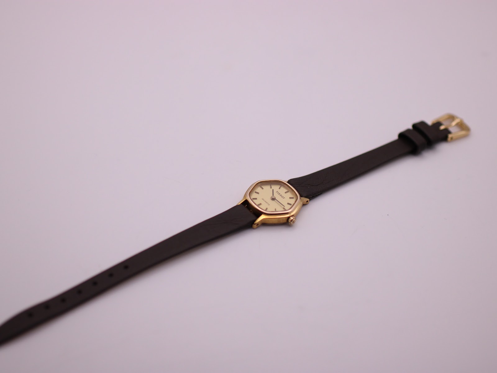 Overhead view of the Tissot watch with its full brown leather strap and gold-coloured buckle against a white background.